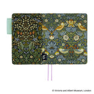 A hardcover notebook or journal featuring a detailed William Morris-style floral and bird pattern. The cover is split vertically into two panels: the left panel has a dark green background with white flowers and small orange flowers, while the right panel has a blue-gray background with yellow birds and white flowers.