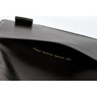 Close-up of a black leather bag interior with gold foil text reading 'Happy Nothing Special Day' and a black leather strap tab visible at the top against a white background.
