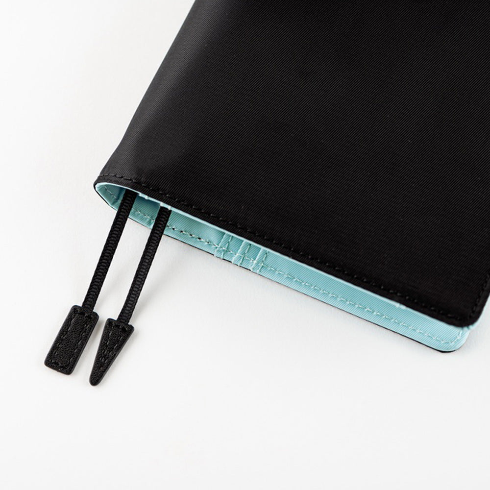 Close-up of a black fabric planner cover with black bookmark ties and a light aqua blue inner lining, shown on a clean white background.