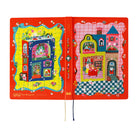 A colorful planner with a bright red cover and open spread showing whimsical illustrated houses and playful scenes. The left page has a yellow background with a blue house, and the right page has a pink background with a blue house.