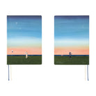 Two hardcover notebooks with illustrated covers are shown side by side on a white background. The covers feature a scenic sunset landscape with a blue sky, stars, a crescent moon, and a grassy field at sunset.