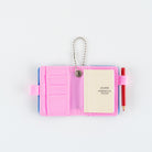 Open small pink notebook keychain with a silver ball chain and a pink loop holding a red pencil, with mini Hobonichi Techo planner inside shown on a plain white background.
