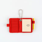 Open small red notebook keychain with a silver ball chain and a red loop holding a yellow pencil, with mini Hobonichi Techo planner inside shown on a plain white background.