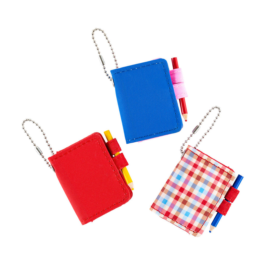 Three small notebook keychains with ball chains on a white background. One is red, one is blue, and one has a red, white, and blue plaid pattern.