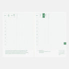 An open planner spread showing two white pages with a light green grid layout, date headers at the top, monthly calendar columns, and text near the bottom. The pages are photographed against a very light gray background.