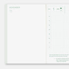 An open planner or calendar showing a blank November month page on the left and a daily gridded page on the right, with a pale mint green border and small printed text.