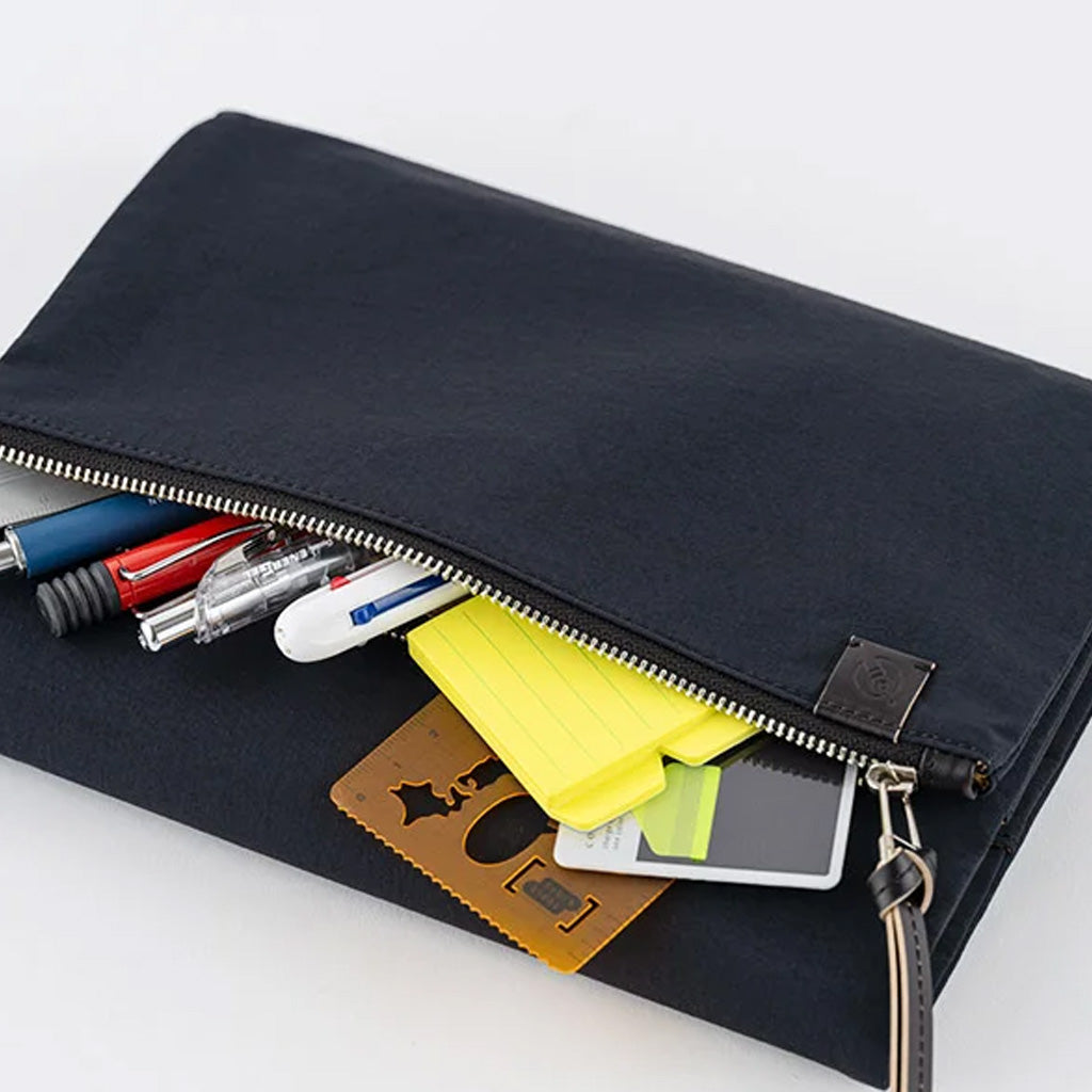 A black canvas zippered pouch shown open, filled with pens, sticky notes, cards, and a small device, photographed on a clean white background.