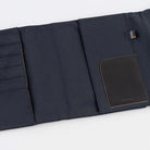 A black fabric notebook cover shown partially unfolded on a clean white background. It features multiple vertical slots on the left, a main pocket on the right and a rectangular black leather pocket.