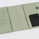 An open sage green fabric notebook cover with multiple compartments, a black leather card holder pocket, and a small black loop tab, photographed on a white background.