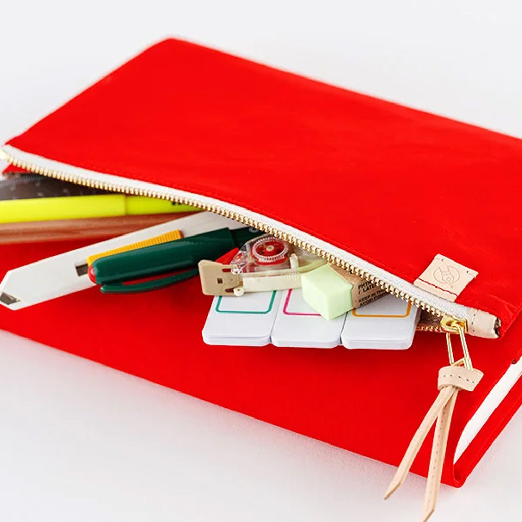 A bright red zippered pouch shown open on a white background, with pens, a ruler, and small office supplies peeking out. A small gold-toned logo tab is visible near the zipper pull.