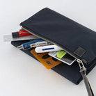 A black nylon zippered pouch shown open with various stationery and utility items peeking out against a clean white background.