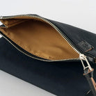 Close-up of an open black pouch showing a tan interior lining and a silver zipper, with a small black brand patch on the side.