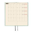 An open planner showing a monthly spread with grid pages, a mint green cover, and ribbon bookmarks, shown on a plain white background.