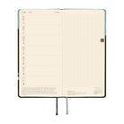 An open planner showing a weekly layout on cream pages. The left page has a vertical weekly schedule with dates and brief notes, and the right page has a light grid for planning.