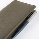 Front of warm gray leather Hobonichi Weeks cover with pen on white background