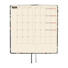 An open planner showing a monthly calendar spread on cream grid pages. 