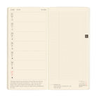 An open cream-colored daily planner showing a weekly layout on the left page and a blank grid section on the right page, photographed against a plain white background.