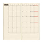 An open planner showing a monthly calendar spread on cream grid paper. 