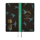 A 2027 daily planner with a black cover decorated with flying teal and purple swallows, featuring a bright green spine and gold foil text.