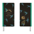 A 2027 planner shown from the front and back on a white background. The cover is black with a teal and purple bird pattern, a teal spine band, and gold text reading 'Natal Design' and '2027 Peace on Earth.