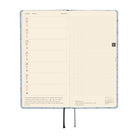 An open weekly planner spread with cream-colored pages. The left-side page has a weekly calendar, while the right page is a grid.
