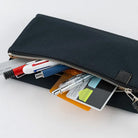 A black fabric zippered pouch shown open on a white background, with pens, a card, and a highlighter partially visible inside.