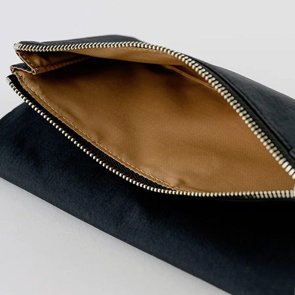 Close-up of a black zippered pouch with a tan interior lining and a silver metal zipper, shown on a light gray background.