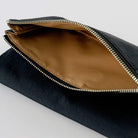 Close-up of a black zippered pouch with a tan interior lining and a silver metal zipper, shown on a light gray background.