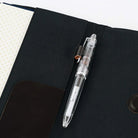A clear transparent ballpoint pen resting in a black fabric organizer pocket next to a notebook.