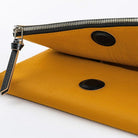 A close-up of a mustard yellow leather notebook cover with a black zipper, black circular snap details, and a black leather zipper pull on a white background.