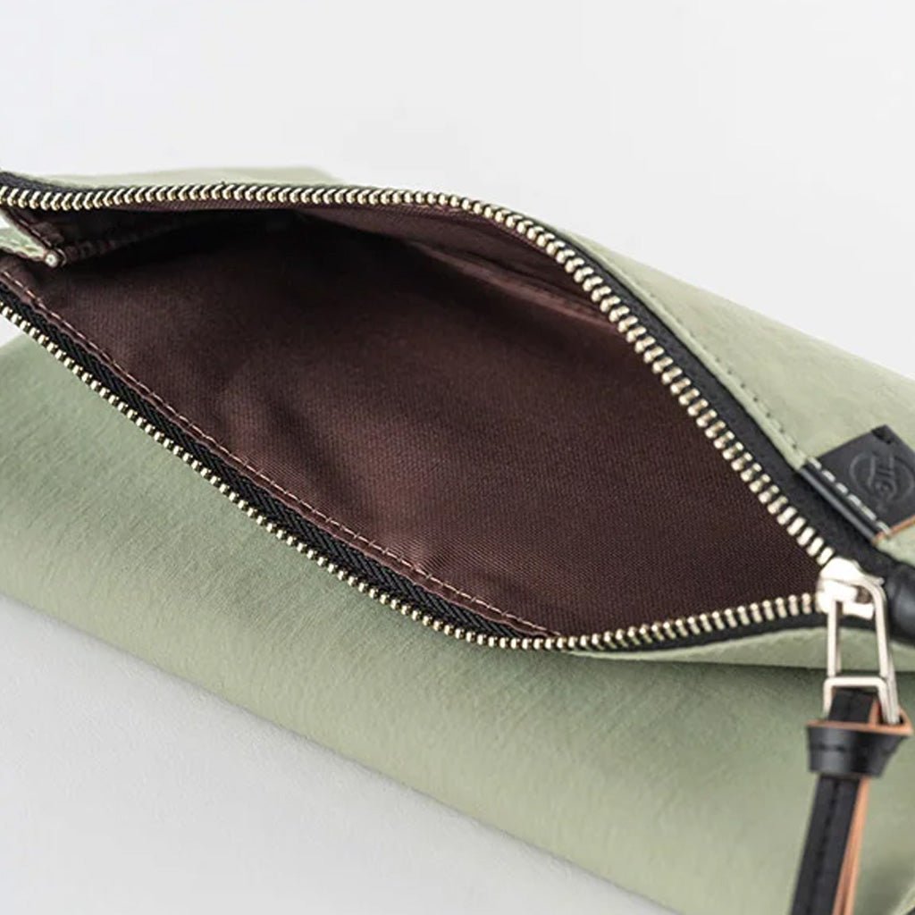 An open sage green leather pouch showing a dark brown satin-lined interior with gold-toned metal zipper teeth and a small black leather brand tab.