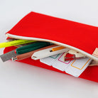 A bright red fabric pencil case with a gold zipper, shown open with various school supplies like pens, a ruler, and sticky notes peeking out, set against a clean white background.