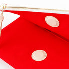 Close-up of a bright red zip pouch with a gold zipper and two circular beige patches on a white background.