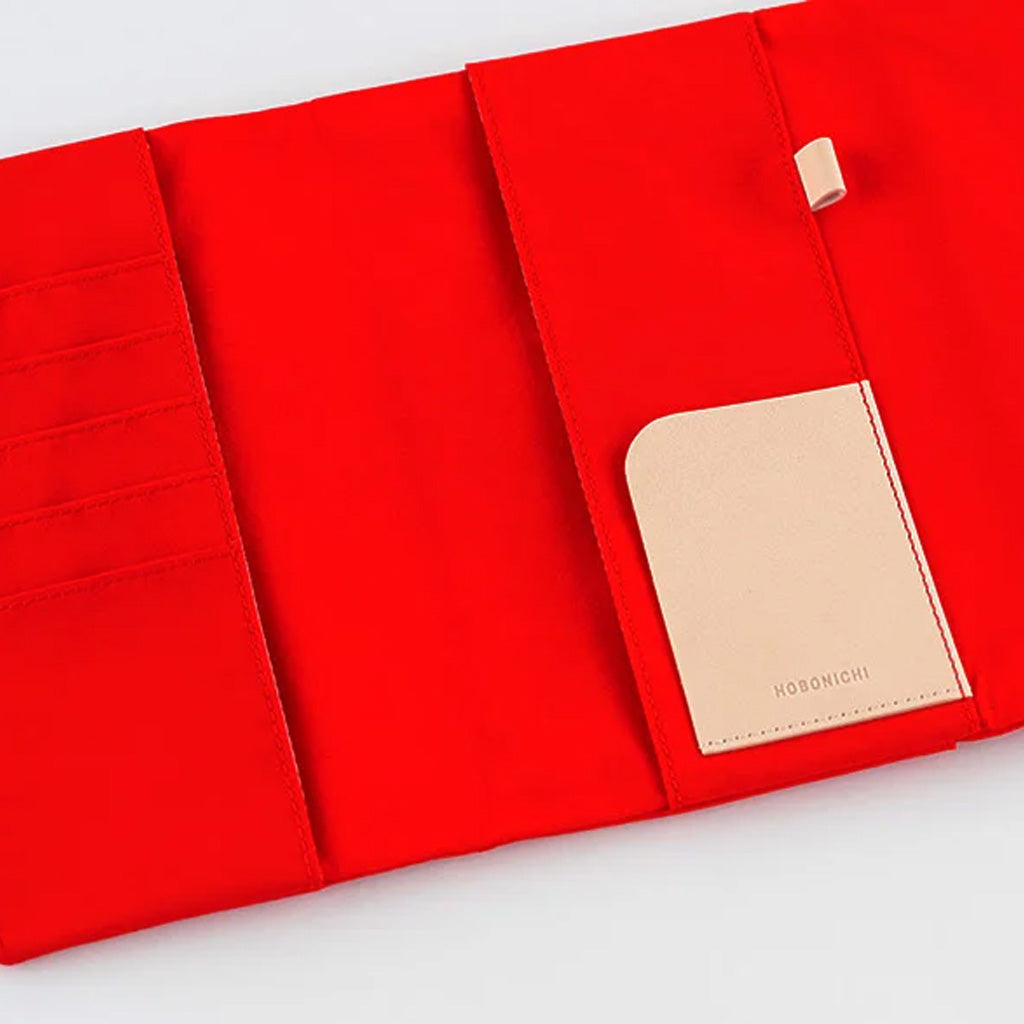 A bright red fabric organizer shown open on a white background, with multiple card slots on the left, a pocket on the right, and a beige leather brand tag reading HOBONICHI.