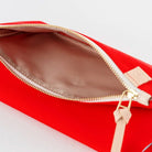 A close-up of a bright red zippered pouch shown open, revealing a beige interior lining and a gold-tone zipper with a small beige pull tab.