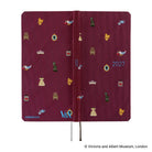 The exterior of a 2027 journal covered in woven "bow & tie" fabric featuring icons from the Victoria & Albert museum collection, such as a crown, teapot, chair, and dress. The back of the cover features the Hobonichi and V&A logos.