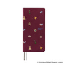 The front of a 2027 journal covered in woven "bow & tie" fabric featuring icons from the Victoria & Albert museum collection, such as a crown, teapot, chair, and dress. 