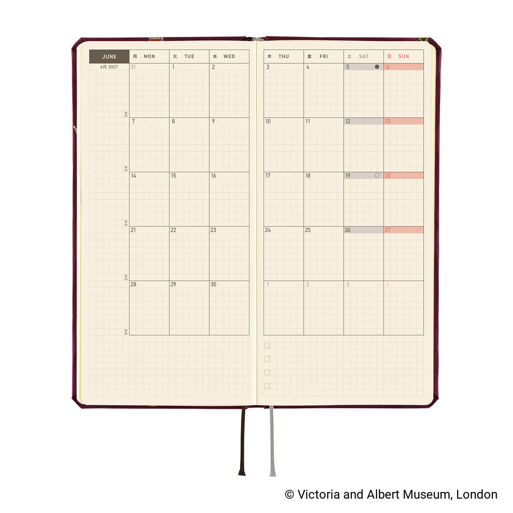 An open planner showing a monthly calendar spread on cream pages with a dark burgundy cover edge and ribbon bookmarks hanging below, photographed on a white background. 