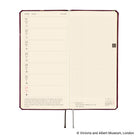An open hardcover planner showing two interior spreads: the left page has a weekly schedule layout with dates from Monday to Sunday, and the right page has a light beige grid. The cover is dark red-brown, and the pages are cream.
