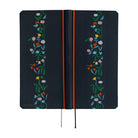 The exterior of a dark navy blue planner with a vertical floral vine design in green, pink, blue, yellow, and white along the right side. It features a bright red band near the spine and ribbon bookmarks hanging from the bottom.
