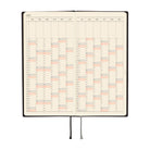 An open 2027 planner with cream-colored pages showing a yearly calendar grid, black binding, and two ribbon bookmarks, photographed on a solid white background.