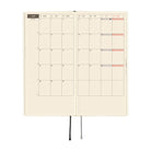 An open planner with a monthly calendar spreadsheet on cream grid paper, shown against a plain white background.