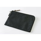 A black zippered pouch with a small leather tassel pull and a small fabric brand tag, photographed on a clean white background.