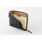 A black zippered pouch with a tan interior, shown open with a notebook and two pens inside, on a clean white background.
