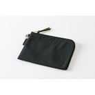 A black A6 zippered Tragen flat pouch on light background