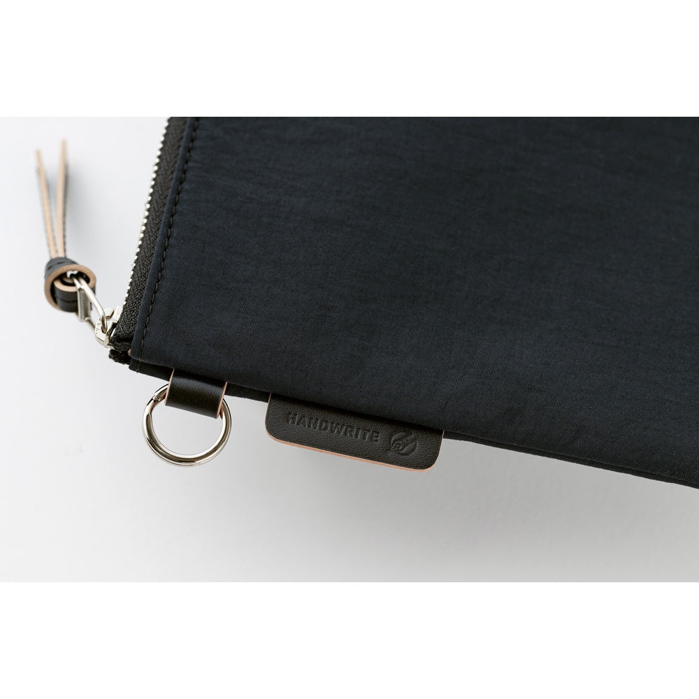 Close-up of a black zip pouch with a silver metal ring and zipper pull, featuring a small black brand tab that reads HANDWRITE on a white background.