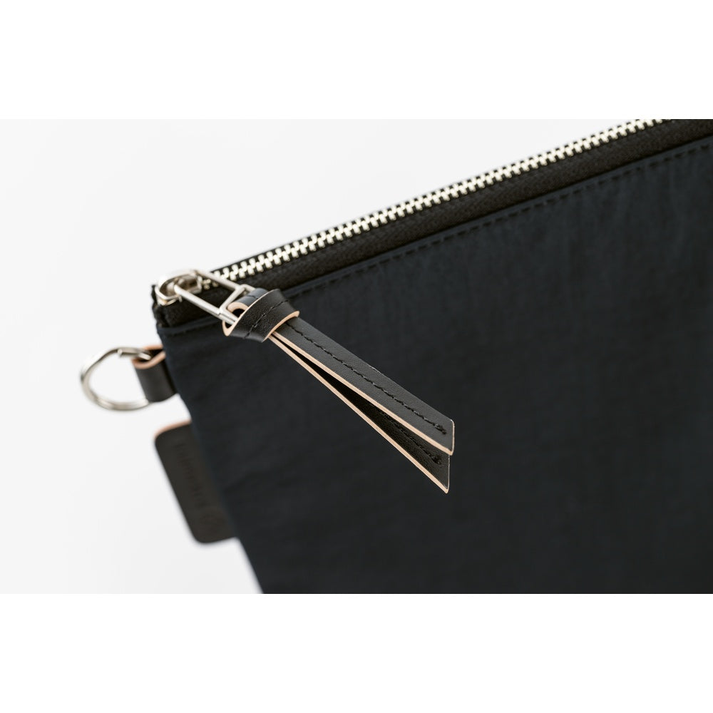Close-up of a black nylon pouch with a silver zipper, a black leather pull tab, and a silver metal keyring on a white background.