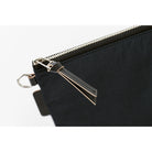Close-up of a black nylon pouch with a silver zipper, a black leather pull tab, and a silver metal keyring on a white background.