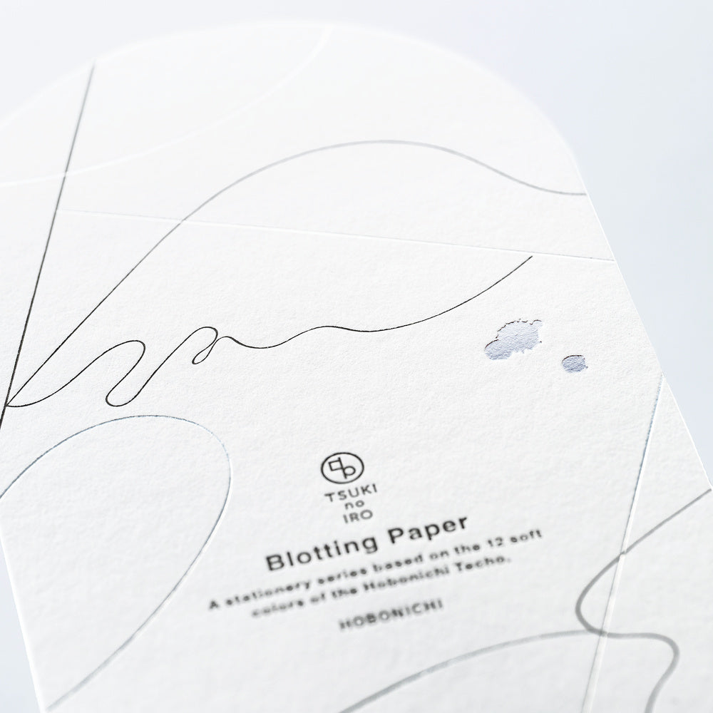A close-up of a sheet of TSUKI no IRO Blotting Paper from the Hobonichi Techo series, featuring fine black line art, subtle gray abstract shapes, and two small blue-gray blotches on a white textured paper background.
