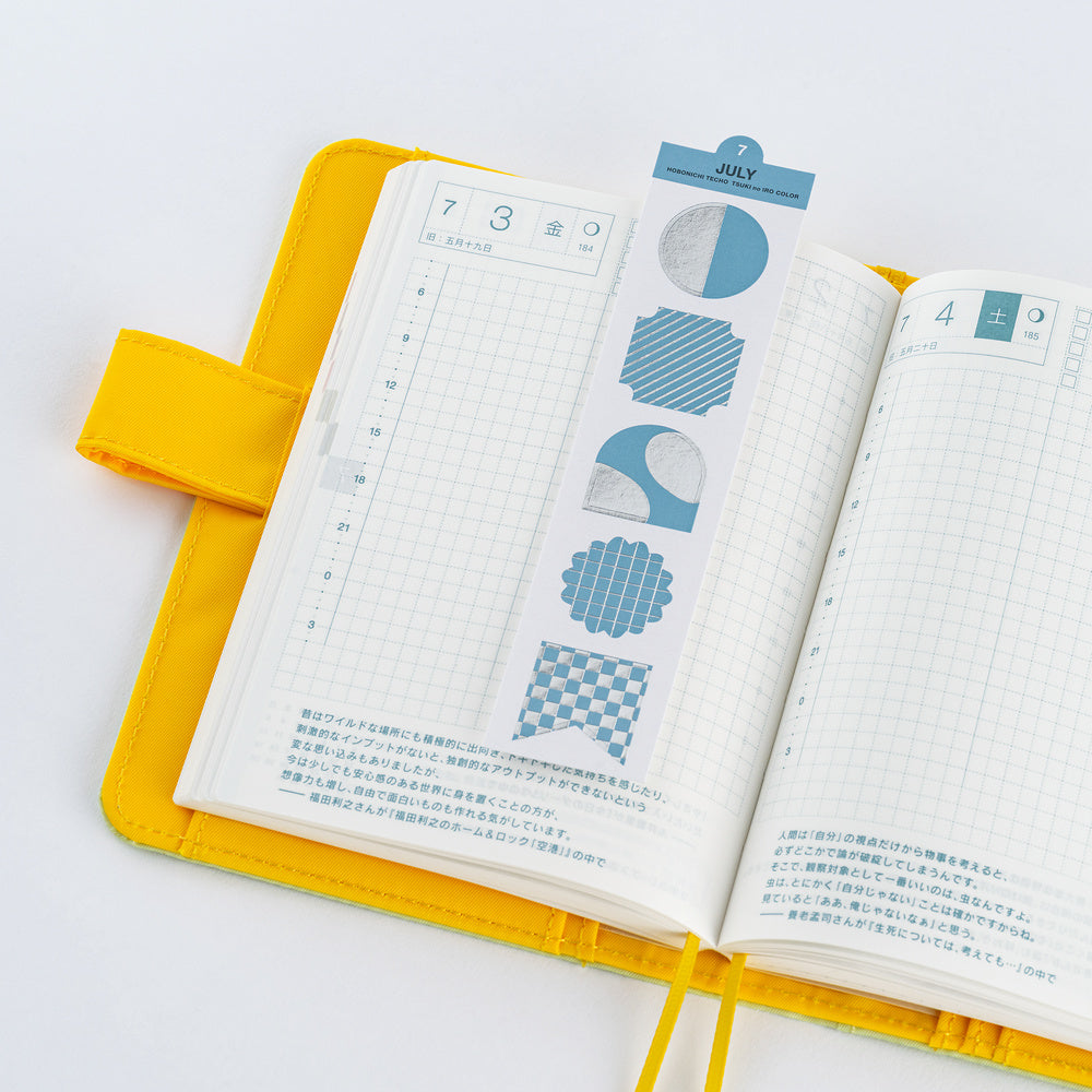 An open yellow planner with grid pages and blue decorative stickers, photographed on a clean white background.